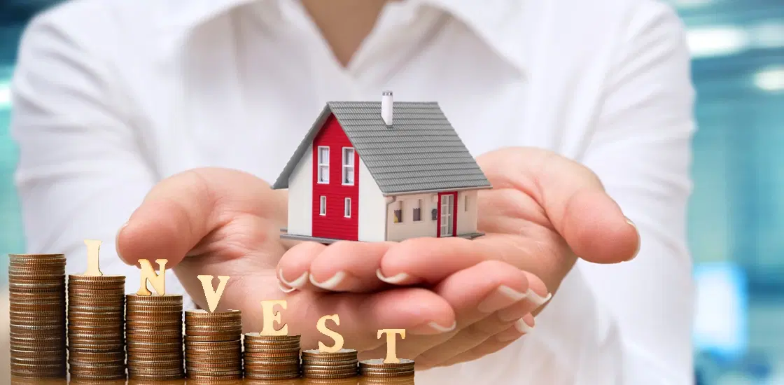Client holding miniature house model and investment coins representing secure wealth creation